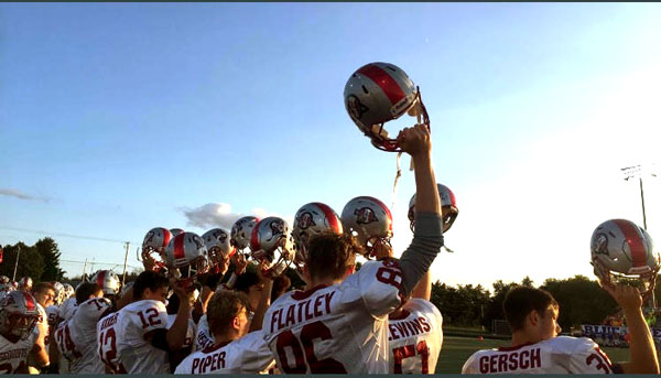 The football team holding their helmets in the air, after honoring our nation.