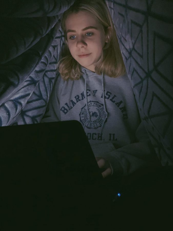 Junior Mickena Prochnow does her homework on the couch under a blanket to stay warm. Needing to clock in five total hours of screen time, students must use their time at home sparingly and not get distracted.