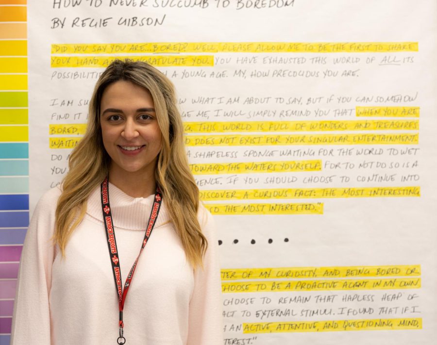 English teacher Jessica Barnes poses in her room next to poem How to Never Succumb to Boredom by Regie Gibson.