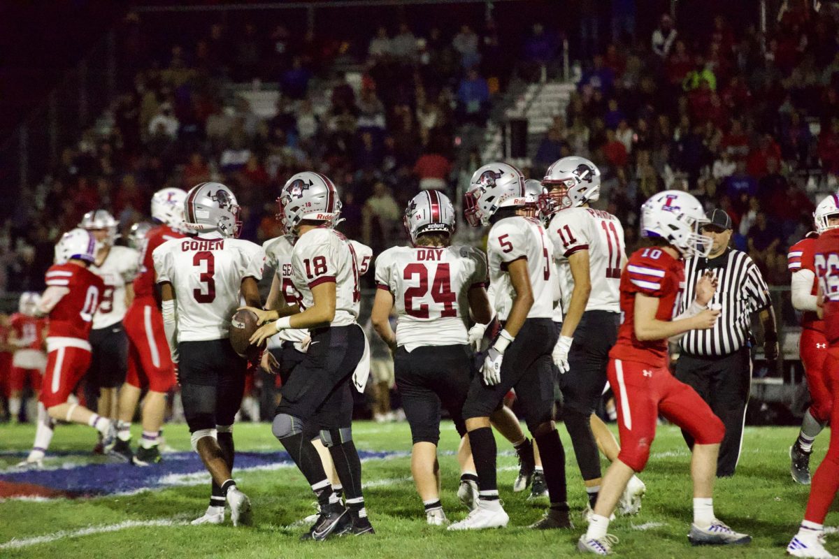 Football team positions themselves on the field, ready to face off against cross town rivals Lakes High School in a thrilling showdown of skill and determination.